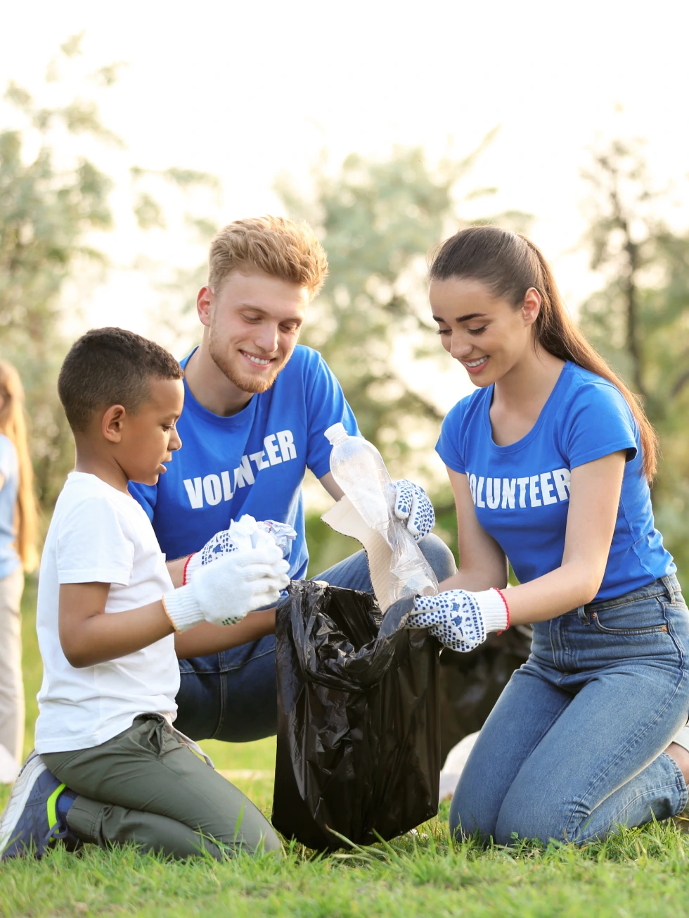 Little African-American boy collecting trash with volunteers in park